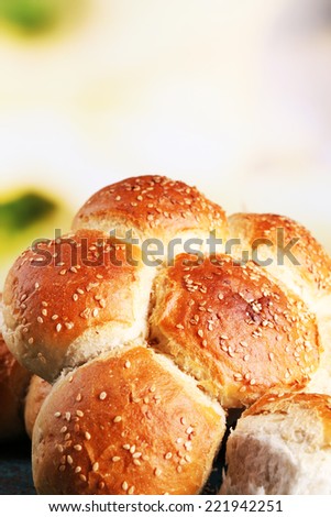 Tasty buns with sesame on color wooden table, on bright background