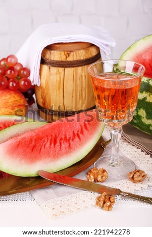 Composition of ripe watermelon, fruits, pink wine in glass and wooden barrel on  color wooden table, on light background