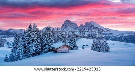 Picturesque landscape with small wooden log cabin on meadow Alpe di Siusi on sunrise time. Seiser Alm, Dolomites, Italy. Snowy hills with orange larch and Sassolungo and Langkofel mountains group Royalty-Free Stock Photo #2219423015