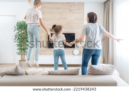 Mother and two daughters having fun jumping on a sofa in living room
