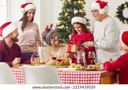 Grandparents giving Xmas gift, present to granddaughter during family Christmas Thanksgiving dinner sitting at table. Happy family on winter holidays. People in Santa hat and New Year interior.