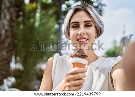 Young caucasian girl eating ice cream making selfie by the camera at the city.