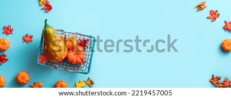 Autumn shopping design concept with shopping cart, maple leaves and pumpkin on blue table background.