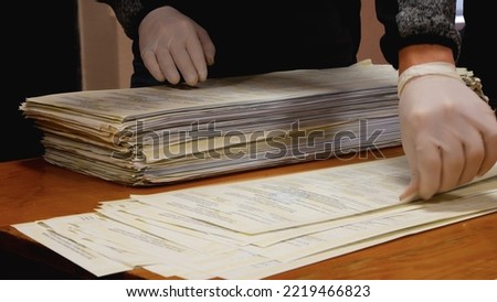 Unrecognizable hands in white gloves recount ballots with votes at the polling station during the election. The concept of democratic voting in elections. Expression of will during elections. 2022 USA Royalty-Free Stock Photo #2219466823