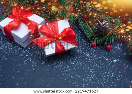    Spruce, fir branches, red berries, gift box on black stone background. Frame border. Christmas New Year composition background. Christmas lights. Space for text                              