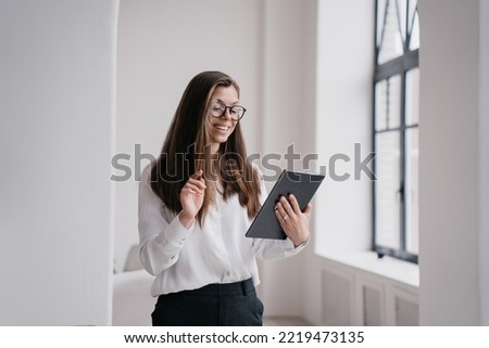 Cheerful young businesswoman using laptop dressed in white shirt and black pants, making video call smiling wide. Beautiful student girl having remote lesson. Successful entrepreneur female at office.
