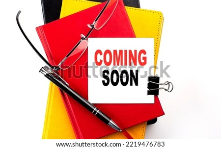 COMING SOON text written on sticky on colorful notebooks