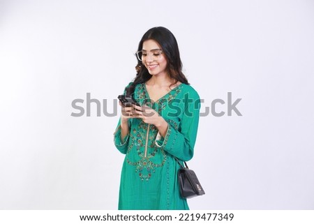 Pakistani girl with long hair casually dressed holding phone looking in phone. Isolated white colour background Royalty-Free Stock Photo #2219477349
