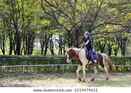 Portrait of smiling female jockey riding horse. Caucasian woman and horse training in the afternoon.