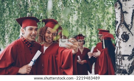 Happy young people girl and guy are taking selfie after graduation ceremony holding diplomas wearing gowns and mortarboards. Photographs, youth and education concept.