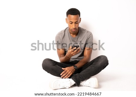 Young african american man sitting on the floor and working in smartphone on white background.