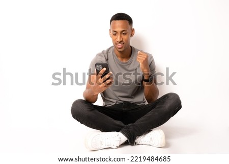 Young african american man sitting on the floor and working in smartphone on white background.