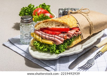 Panini sandwich with ham, crispy salad and vegetables. Healthy food to go concept, lunch or snack option. Trendy hard light, dark shadow, stone concrete background, close up