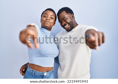 Young african american couple standing over blue background pointing to you and the camera with fingers, smiling positive and cheerful 