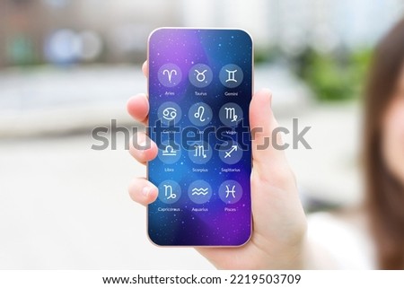 A woman's hand holds a smartphone with an astrological application on the background of the street, astro forecast for all zodiac signs