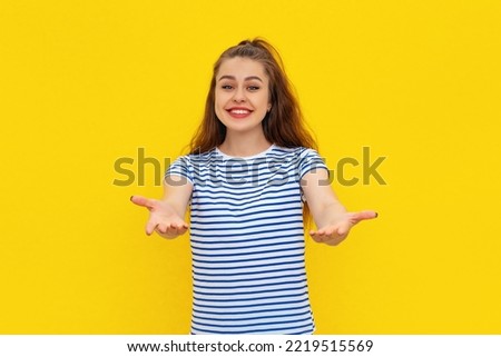 Come into my arms. Portrait of friendly and cute charming girl stretching hands and looking forward with happy smile to cuddle and welcome guests, standing in striped t shirt over yellow background