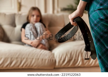 Mother wants to punish her child daughter with belt in hand. Angry mom punishes teen girl for offense and hits baby with belt. Concept of family quarrels, problems and parenting. Copy text space Royalty-Free Stock Photo #2219522063