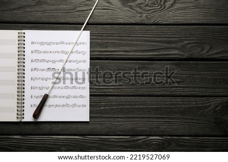 Conductor's baton and sheet music book on black wooden table, top view. Space for text