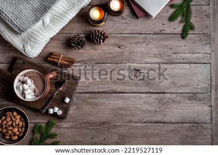 Hot coffee drink, almonds, cosy knitted sweater on wooden background with candles and pine cones, copy space. Hygge and home comfort concept. Seasonal winter cosy composition.