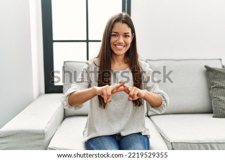 Young latin woman talking with sign language sitting on sofa at home
