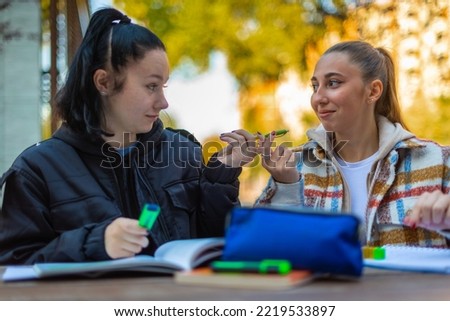 A female high school student is giving a pen to her friend Royalty-Free Stock Photo #2219533897