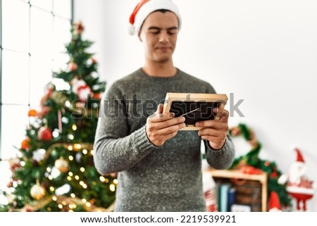 Young hispanic man looking photo standing by christmas tree at home