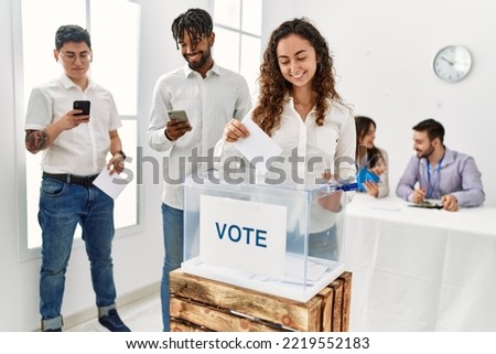 Young voter woman smiling happy putting vote in voting box at electoral center.