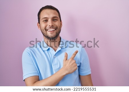 Hispanic man standing over pink background cheerful with a smile on face pointing with hand and finger up to the side with happy and natural expression 