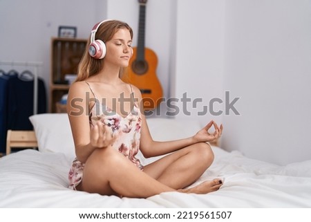 Young blonde girl doing yoga exercise sitting on bed at bedroom