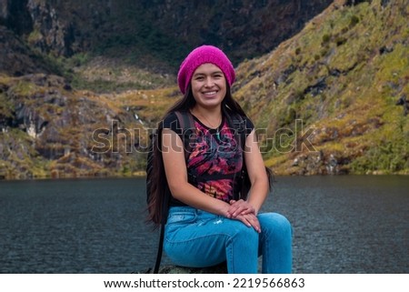 Attractive happy hiker sitting on a rock next to a tranquil lake in the beautiful mountains