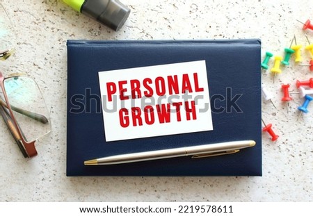 Text PERSONAL GROWTH on a business card lying on a blue notebook next to the glasses and stationery. Business concept.