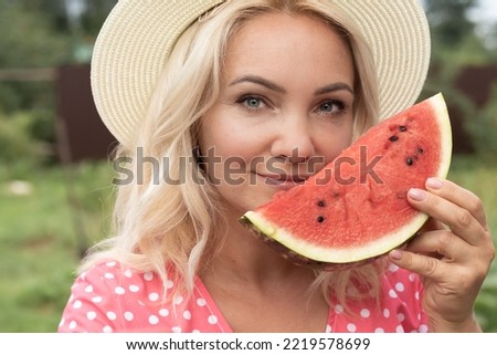 Photo of a young blonde woman in a hat and pink dress. who eats juicy delicious watermelon, biting off pieces of her favorite fruit. Daylight saving time and the concept of nutrition.