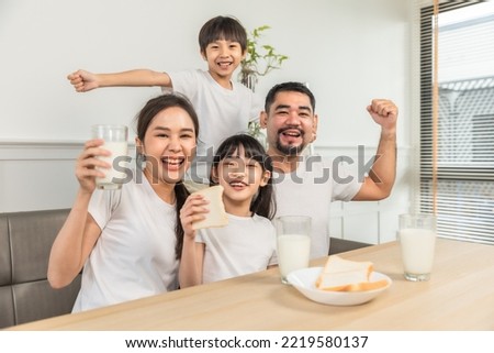 Asian  family enjoying breakfast at living room. little girl daughter sitting on table, drinking milk with smiling father and mother in morning. Happy family at home. Royalty-Free Stock Photo #2219580137