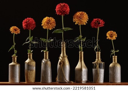 Row of homemade vases from bottles with red and yellow zinnia flowers on a dark background