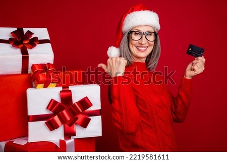 Photo of grandma hold credit card direct finger pile gift wear specs hat pullover isolated red color background