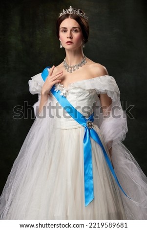 Young queen. Portrait of adorable girl in image of medieval royal person in renaissance style dress isolated on dark background. Comparison of eras, beauty, history, art. Historical reconstruction. Royalty-Free Stock Photo #2219589681