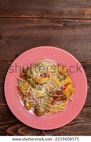 Funchoza with chicken and vegetables in teriyaki sauce garnished with sesame seeds in a plate on a wooden table.copy space Vertical photo