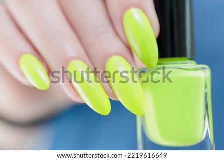 Female hand with long nails and neon yellow green manicure with bottles of nail polish