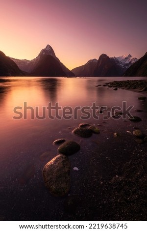Intense twilight colors glow in the clear morning sky over the Milford Sound of New Zealand in the Fiordland National Park. Royalty-Free Stock Photo #2219638745