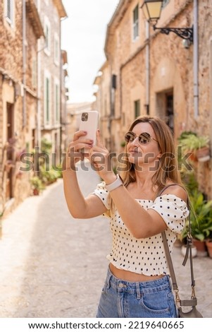 Young tourist woman using smartphone in the city, taking pictures. Girl makes a photo on the streets of the old town on a summer sunny day. Girl using cell phone photography app.