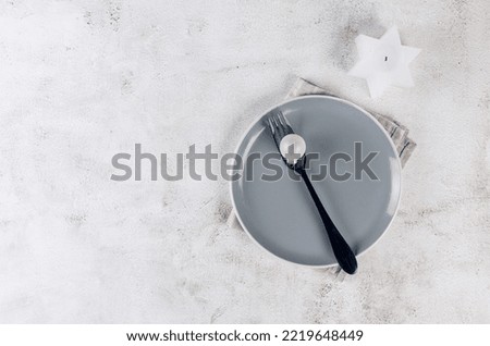 Christmas table setting. Top view of empty grey plate with black cutlery and craft wooden decorations on light table. Event table decoration. 