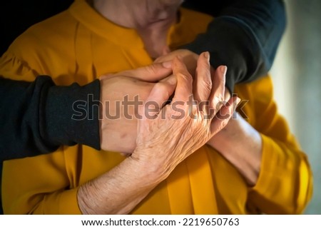 A young man, a volunteer, a son carefully hugs his beloved grandmother, supports and helps an elderly woman in retirement, his grandparent. Young male and female elderly hands with wrinkles closeup.  Royalty-Free Stock Photo #2219650763