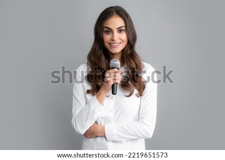 Beautiful business woman is speaking on conference. Stylish girl singing songs with microphone, holding mic at karaoke, posing against gray background.