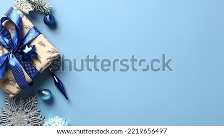 Christmas gift box with blue ribbon bow, snowy fir branches, ornaments on pastel blue background. Flat lay, top view.