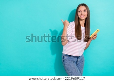 Photo of adorable positive nice girl with straight hairdo striped t-shirt directing look empty space isolated on teal color background