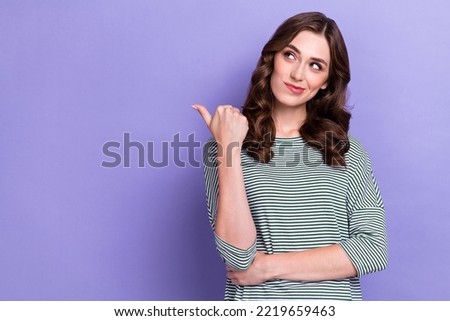 Portrait photo of dreaming positive girl pouted lips recommend option finger directing empty space product isolated on purple color background