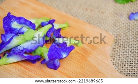 Selected focus Pile of butterfly pea flowers (Clitoria ternatea) on wodden board and burlap,  Telang flower for herbal tea raw materials - Photo product concept on photo studio with blur background