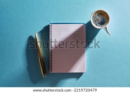 blank note cup of coffee and gold pen against blue background