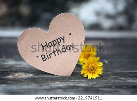 Happy Birthday text on paper card with flower decoration on wooden background
