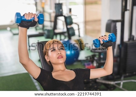 A young and attractive asian woman does alternating incline dumbbell bench presses. Working out chest and upper body at the gym. Royalty-Free Stock Photo #2219744391
